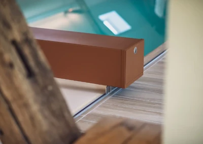 chez-alexandra-and-damien-2 Boîtier rectangulaire marron fixé sur un rail en métal, posé sur un sol en bois clair, avec une piscine en arrière-plan.