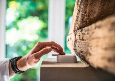 chez-alexandra-and-damien-4 Main appuyant sur un interrupteur blanc monté sur un mur en bois, avec une fenêtre floue en arrière-plan.