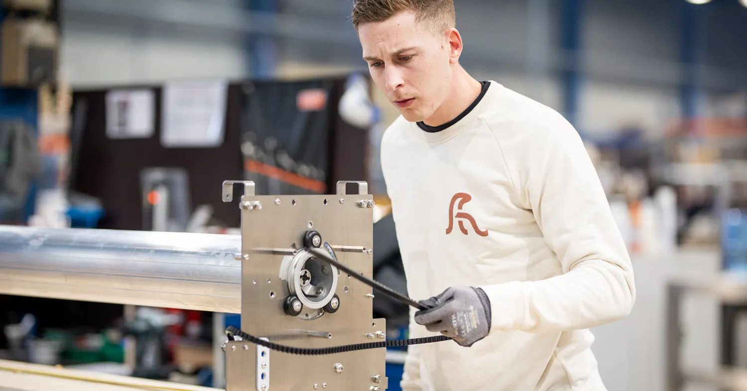 COVERSEAL-entreprise-1 Un homme en pull blanc travaille sur une machine métallique dans un atelier industriel lumineux.