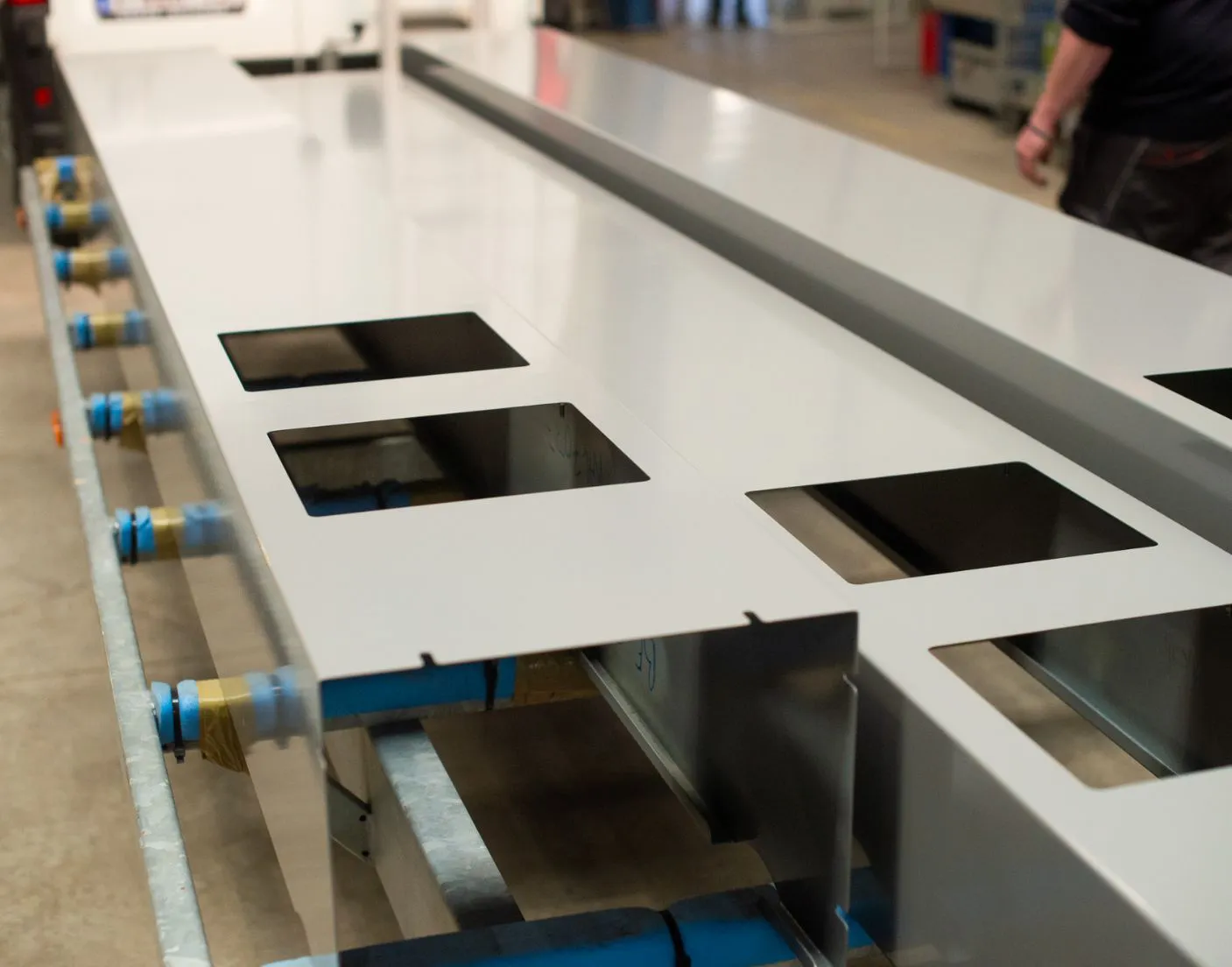 COVERSEAL-entreprise-2 Plaques métalliques grises avec découpes carrées sur un support industriel, dans un environnement d'atelier.