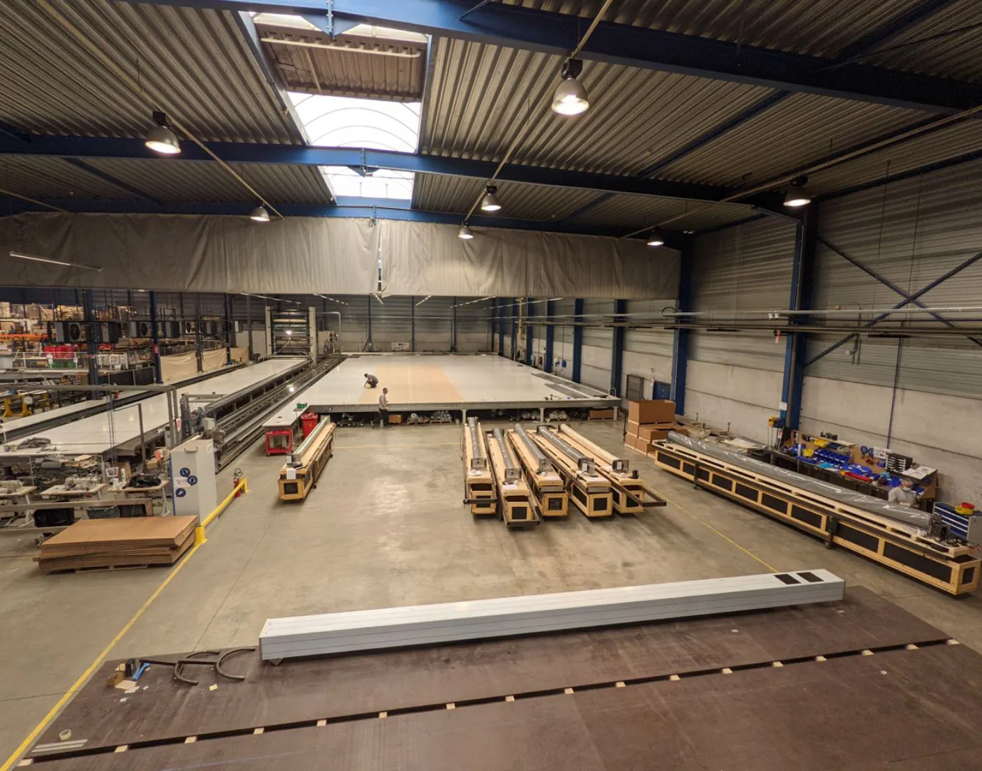 COVERSEAL-entreprise-4 Intérieur d'une usine avec de grandes machines alignées sur le sol en béton, sous un toit en tôle ondulée avec éclairage suspendu.