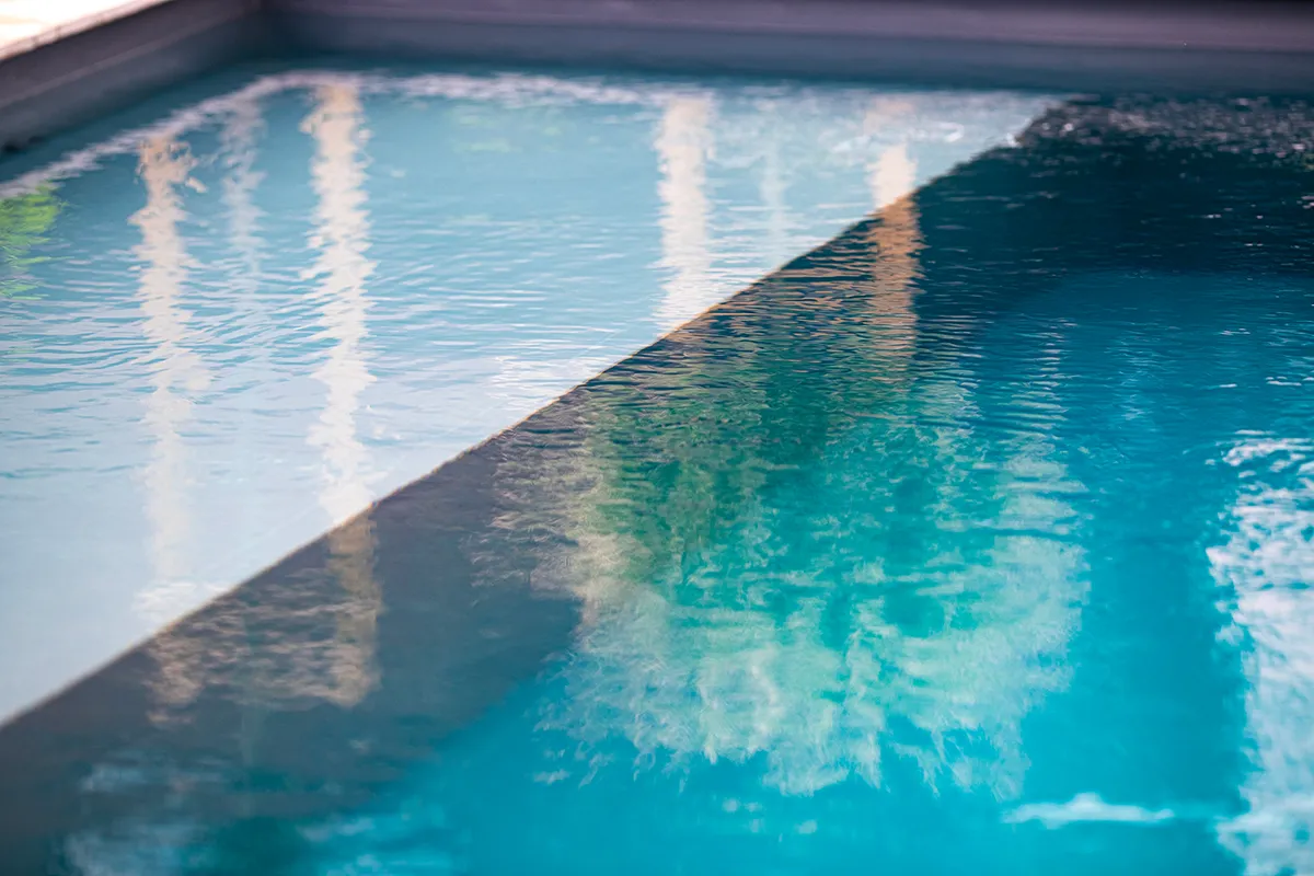 DESIGN-GARDEN-(25) Surface d'une piscine avec de l'eau claire et des reflets de structures environnantes visibles.