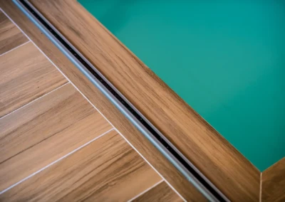 chez-alexandra-and-damien-6 Vue rapprochée d'un bord de piscine en bois avec une couverture en verre turquoise.