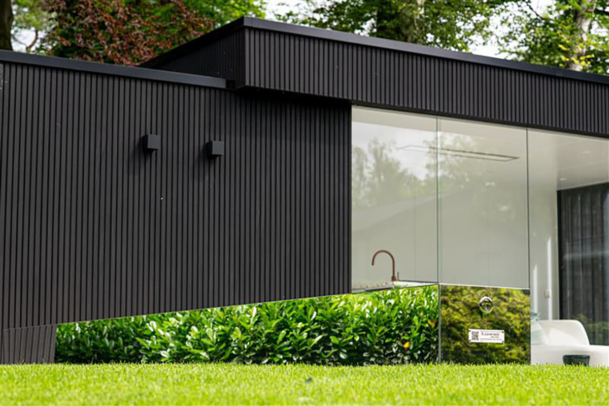 image (76) Une maison moderne en bois sombre avec de grandes fenêtres en verre, entourée de verdure et d'une pelouse verte.