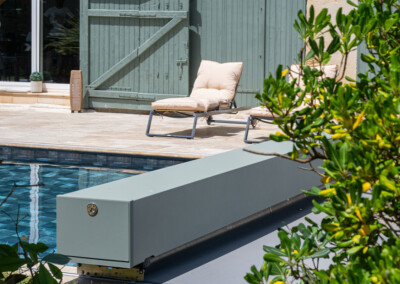 Sequoia3 Gros plan sur l'habillage de la Coverseal grise au bord de la piscine, avec en arrière-plan les transats et la maison en pierre.