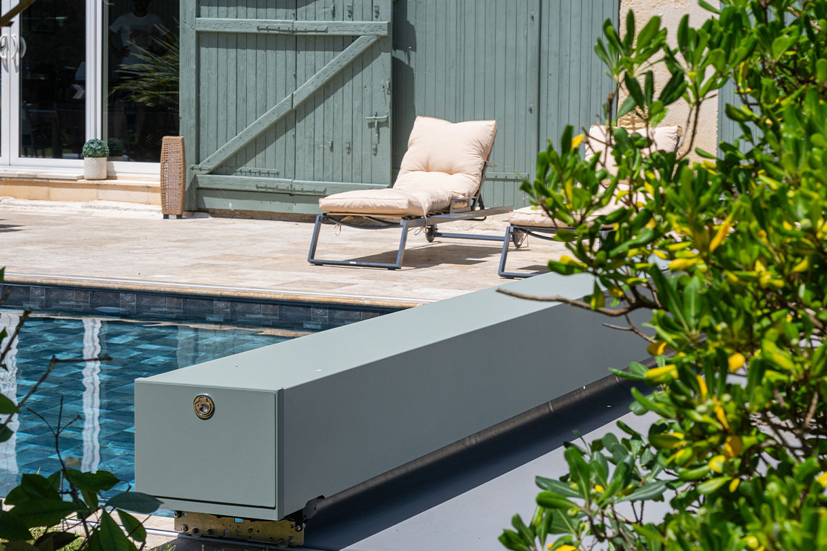 Sequoia3 Gros plan sur l'habillage de la Coverseal grise au bord de la piscine, avec en arrière-plan les transats et la maison en pierre.