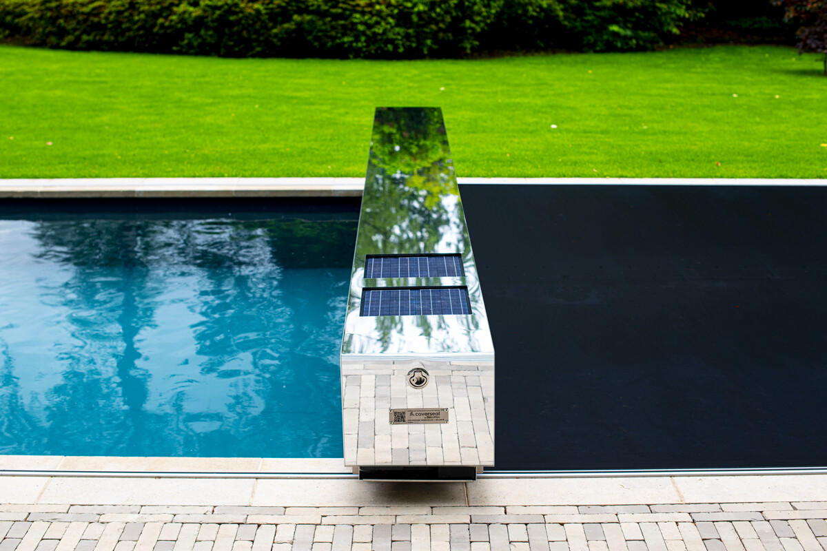 Eine silberne Poolabdeckung mit Solarpanelen, umgeben von grünem Rasen, teilweise über einem blauen Pool ausgefahren.